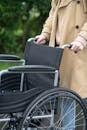 A person in a coat holds the handles of a wheelchair outdoors, illustrating accessibility and support.
