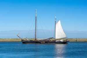 A tranquil image of a sailing boat cruising along a calm sea under a blue sky.